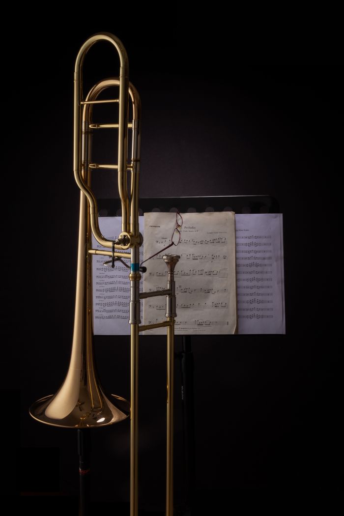 A trombone standing beside sheet music in a dark studio, showcasing musical artistry.